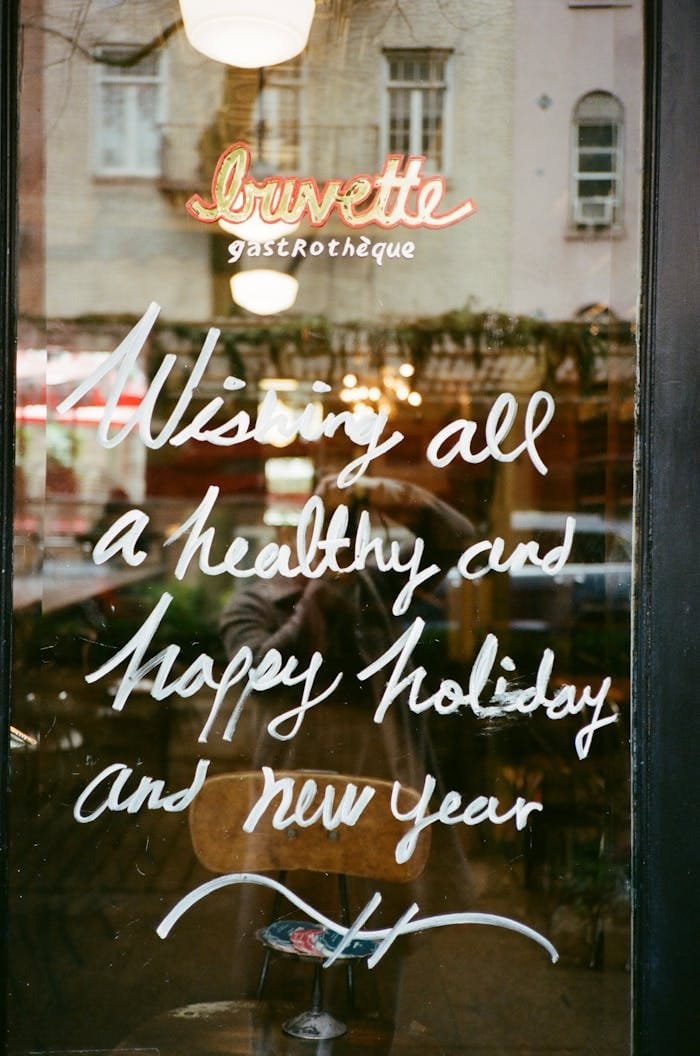 Colorful holiday message on a restaurant window reflecting the city lights.