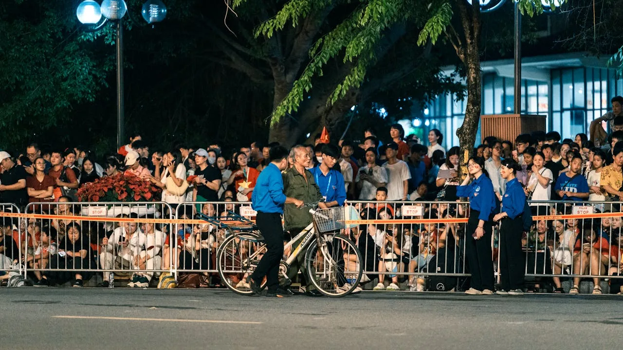 A crowd gathered on a street in Hanoi at night for a public event, featuring barriers and bicycles.