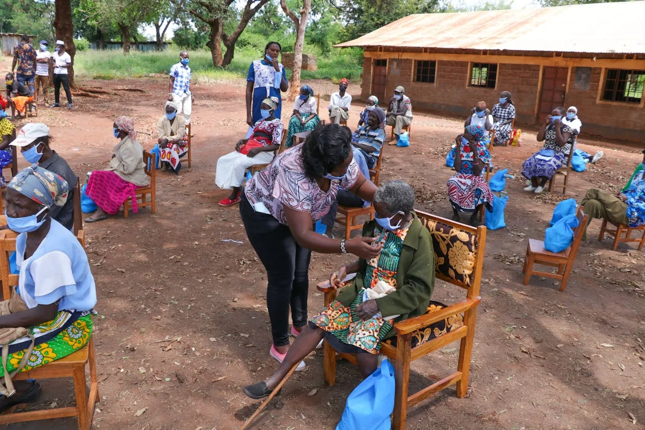 Aid workers assist elderly people with healthcare support in a rural setting.