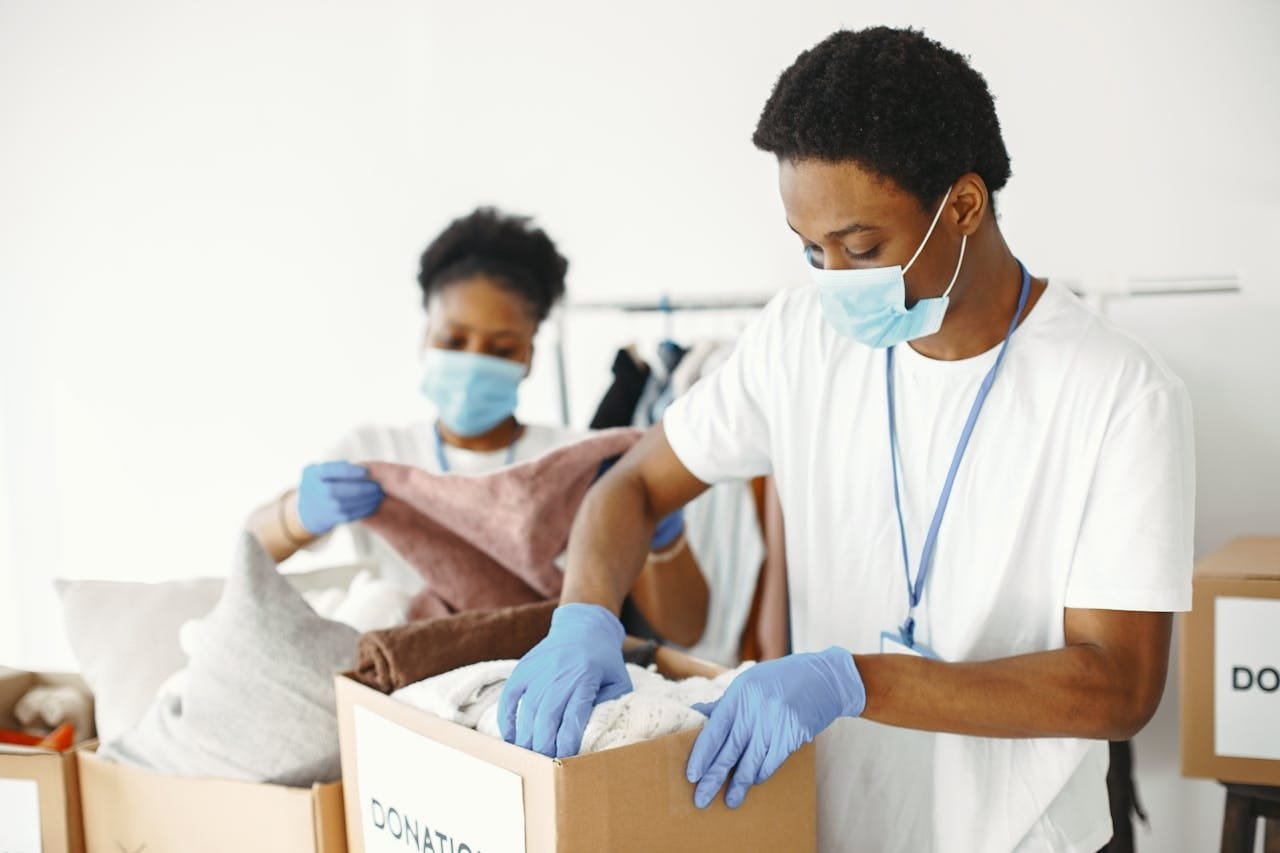 Adults wearing masks and gloves sorting donations for charity indoors.