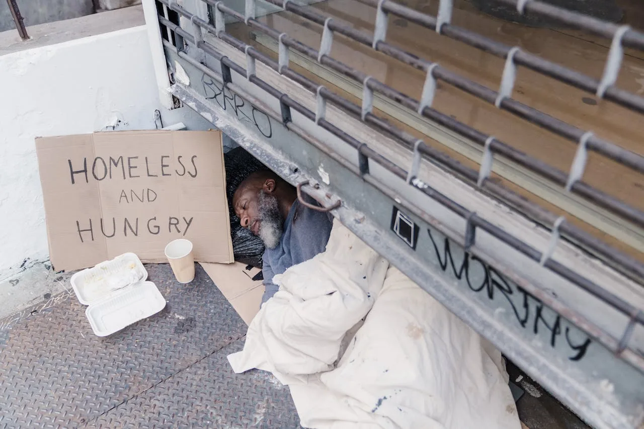 A powerful depiction of a homeless man sleeping with a sign reading 'Homeless and Hungry.'